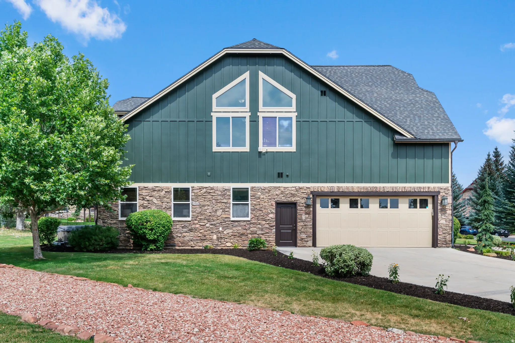 Multi-level exterior featuring a stone facade, vertical siding, a two-car garage, and multiple window styles