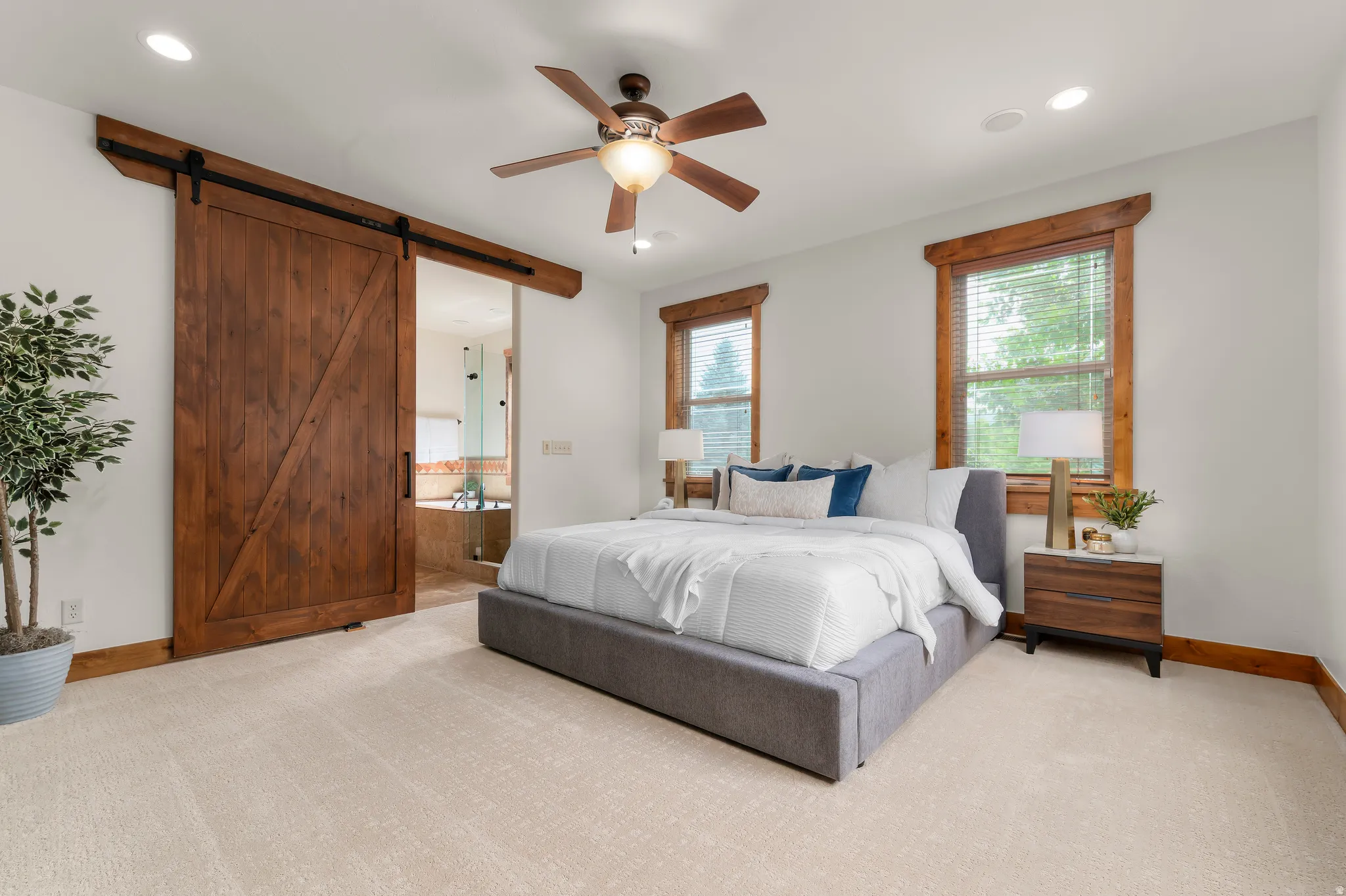 Wood-finish barn door, recessed lighting, ceiling fan, wood-trimmed windows, and light-toned carpeting