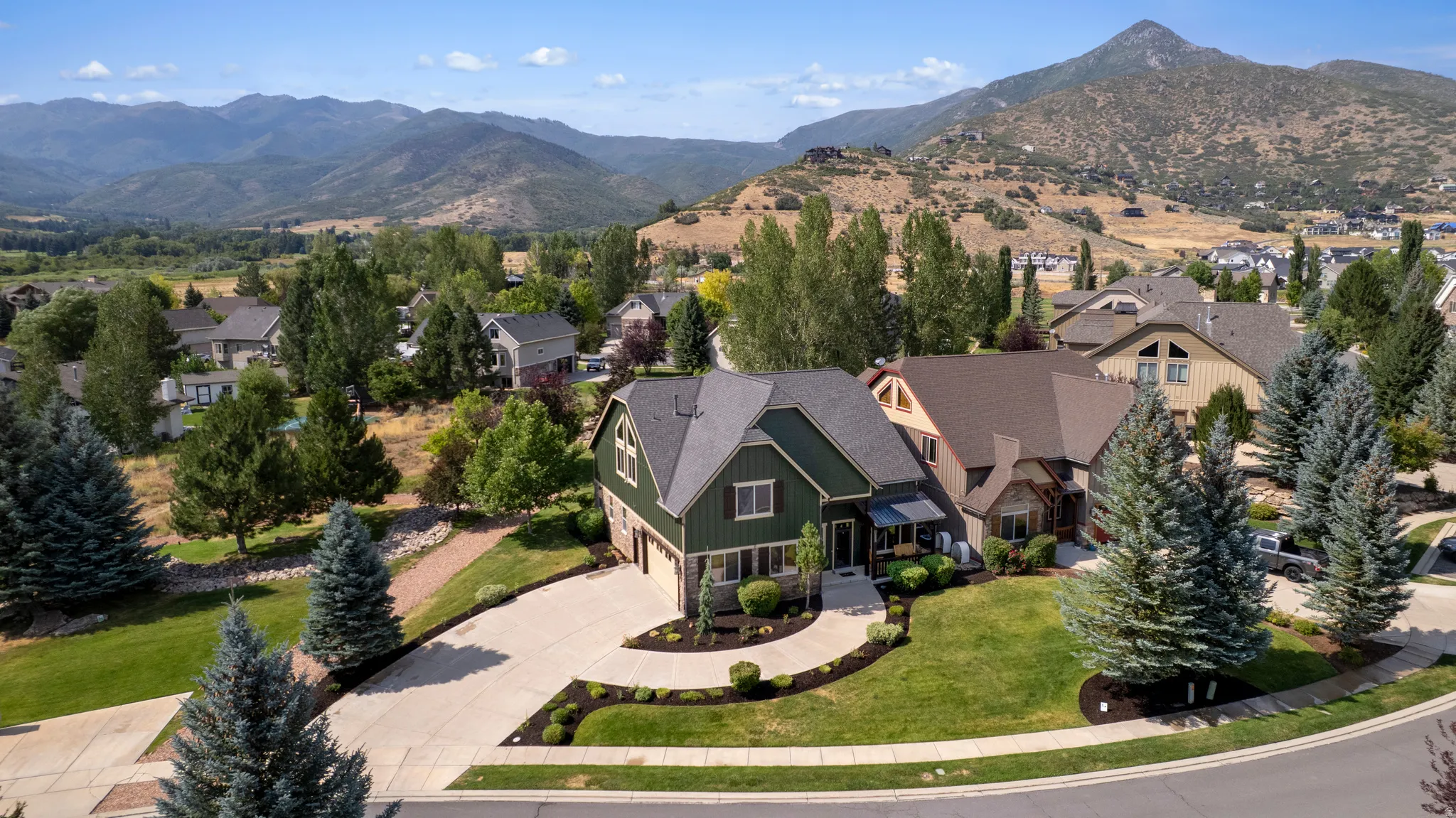 Gabled roofline, dark green siding, attached two-car garage, mature landscaping, and a concrete driveway
