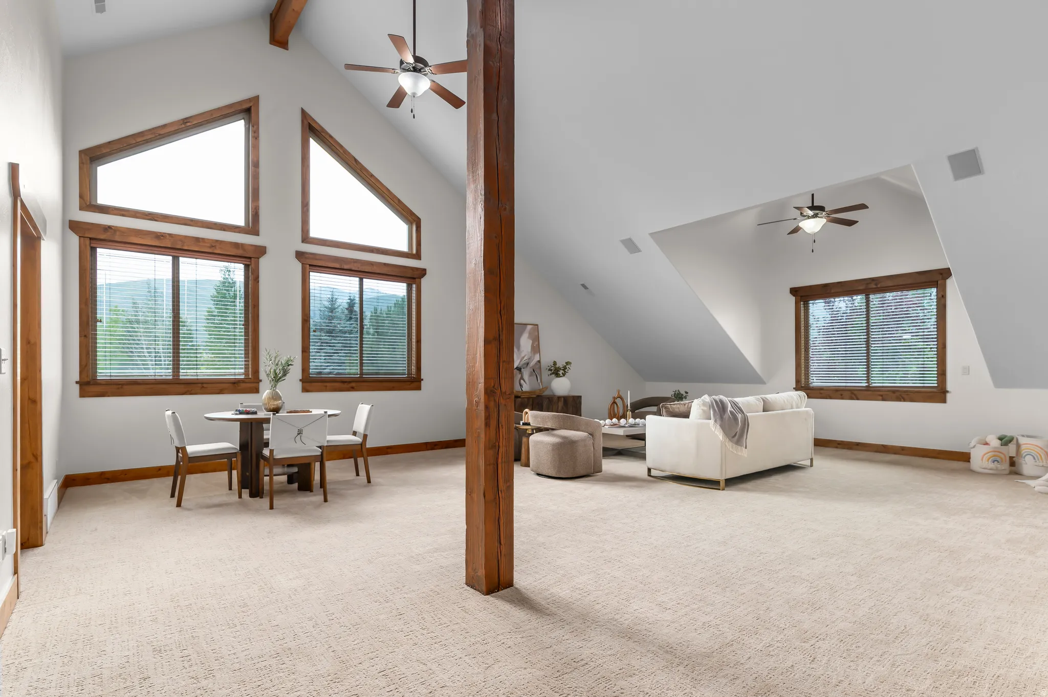 Vaulted ceiling with exposed wood beams, multiple large windows with wood trim, wall-to-wall carpeting, and multiple ceiling fans