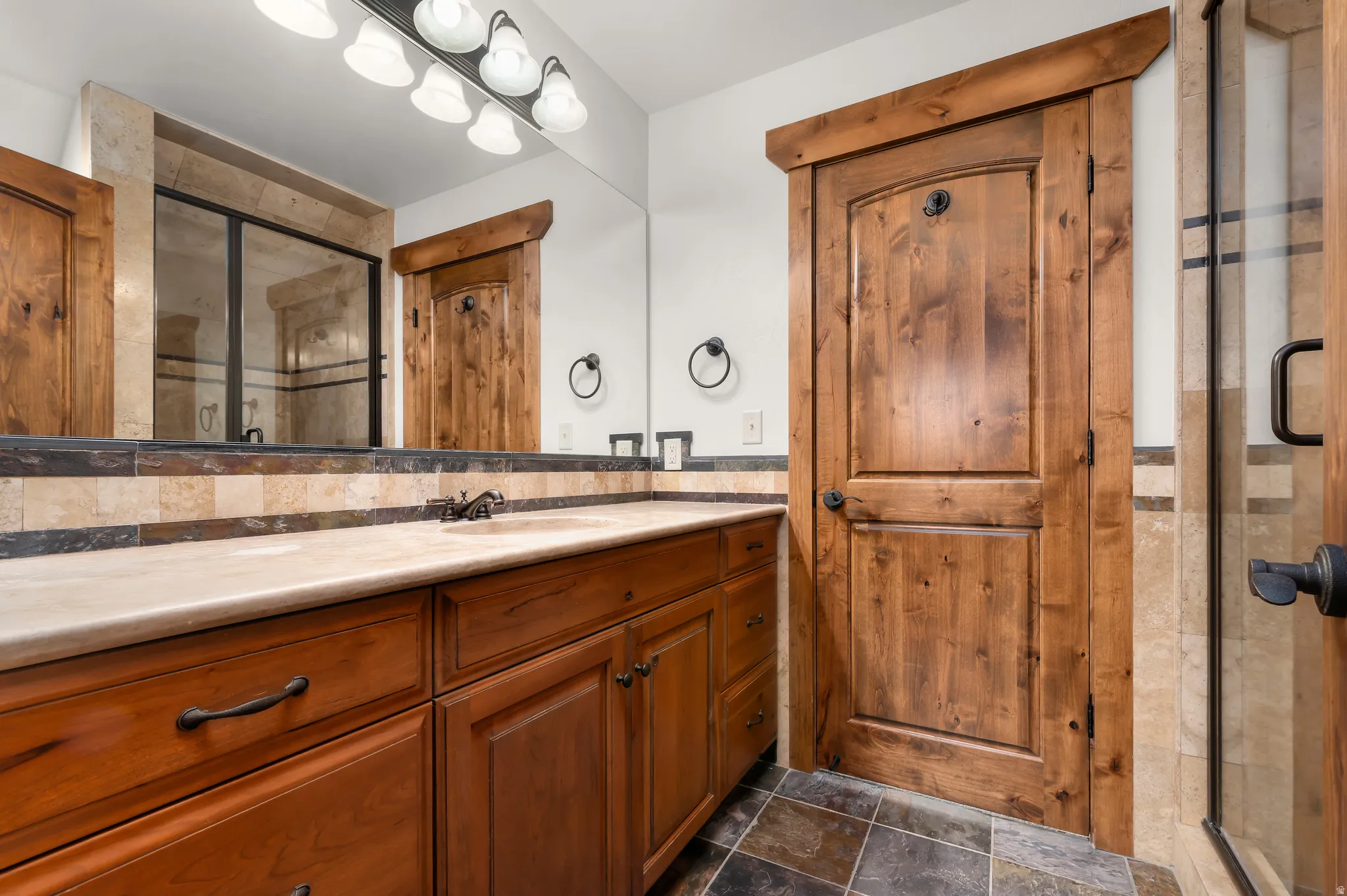 Wood-finish vanity with an integrated sink, stone countertop, and tile backsplash
