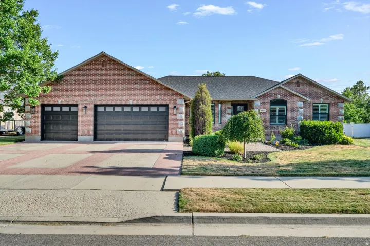 Brick exterior with stone accents, two-car garage with dark paneled doors, patterned paver driveway, front landscaping, and a dark shingle roof