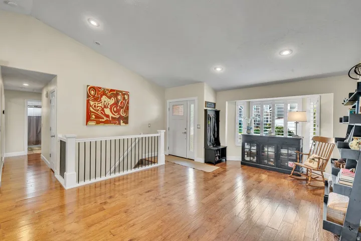 Vaulted ceiling, recessed lighting, wood-finish flooring, white bay window shutters, and a white front entry door with glass inserts