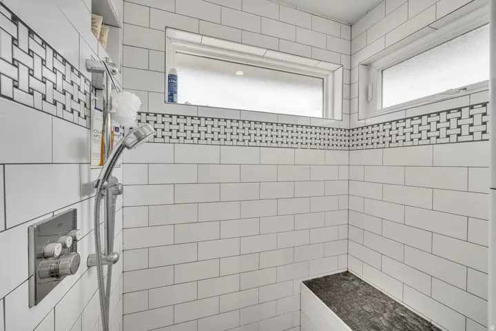 Shower featuring white subway tile, a decorative mosaic tile band, two frosted privacy windows, a built-in shower bench, and a modern shower system