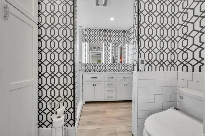 White vanity with dual sinks, two illuminated mirrors, and a light wood-finish flooring
