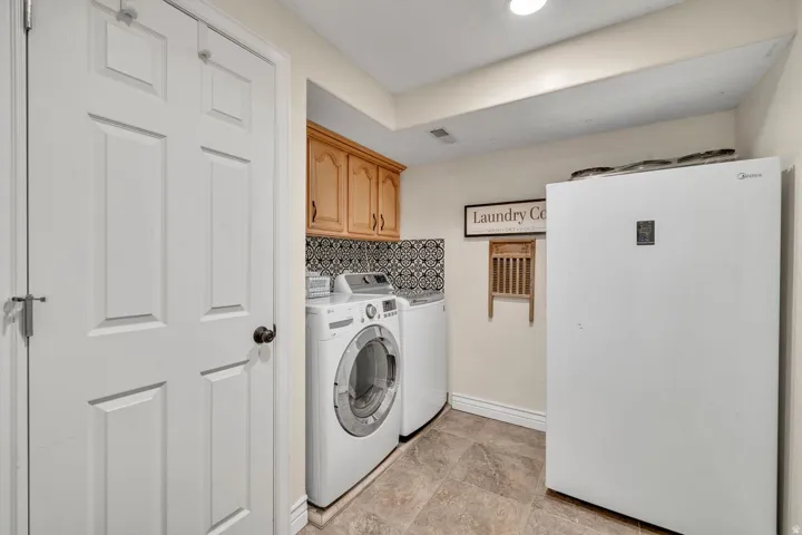 Integrated washer and dryer, patterned tile backsplash, wood-finish cabinetry, and tiled flooring