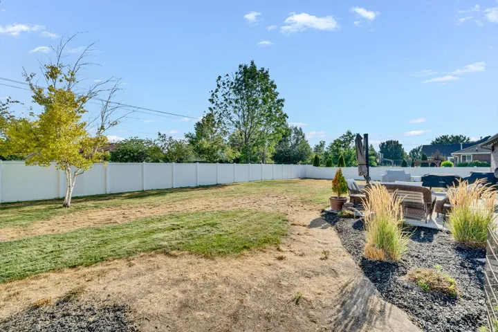 Expansive backyard featuring a white privacy fence, mature trees, and a landscaped rock garden