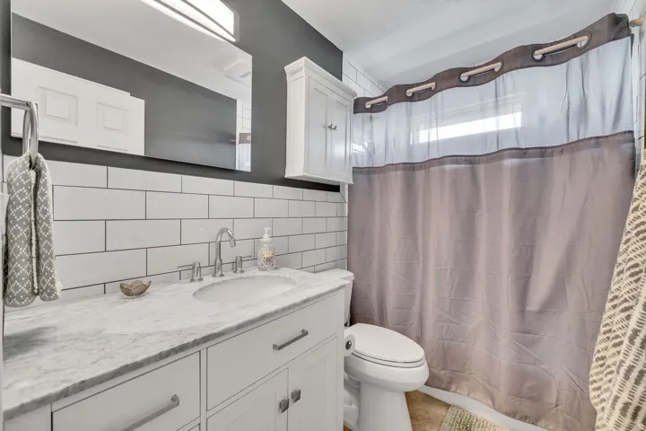 White subway tile backsplash, white vanity with integrated sink, polished chrome faucet, built-in wall cabinet, and overhead light fixture