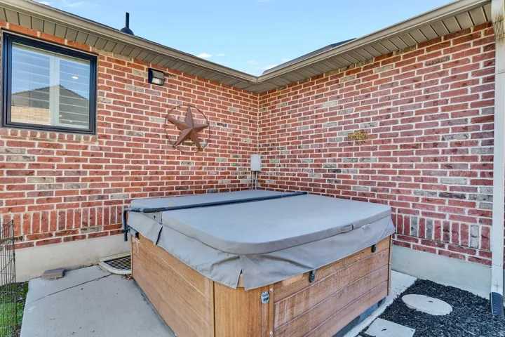 Exterior brick wall with an outdoor spa featuring a wood-finish cabinet and grey cover, positioned on a concrete patio