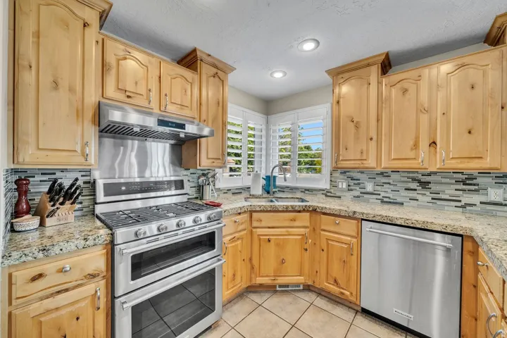 Kitchen featuring natural wood cabinetry, granite countertops, tile backsplash, stainless steel appliances, and recessed lighting