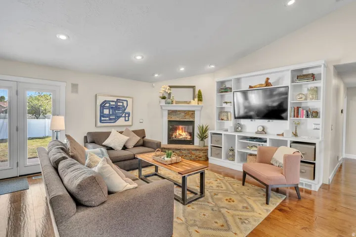 Living area featuring a fireplace with stone surround, custom built-in shelving, recessed lighting, wood-finish flooring, and French doors leading to a private outdoor space