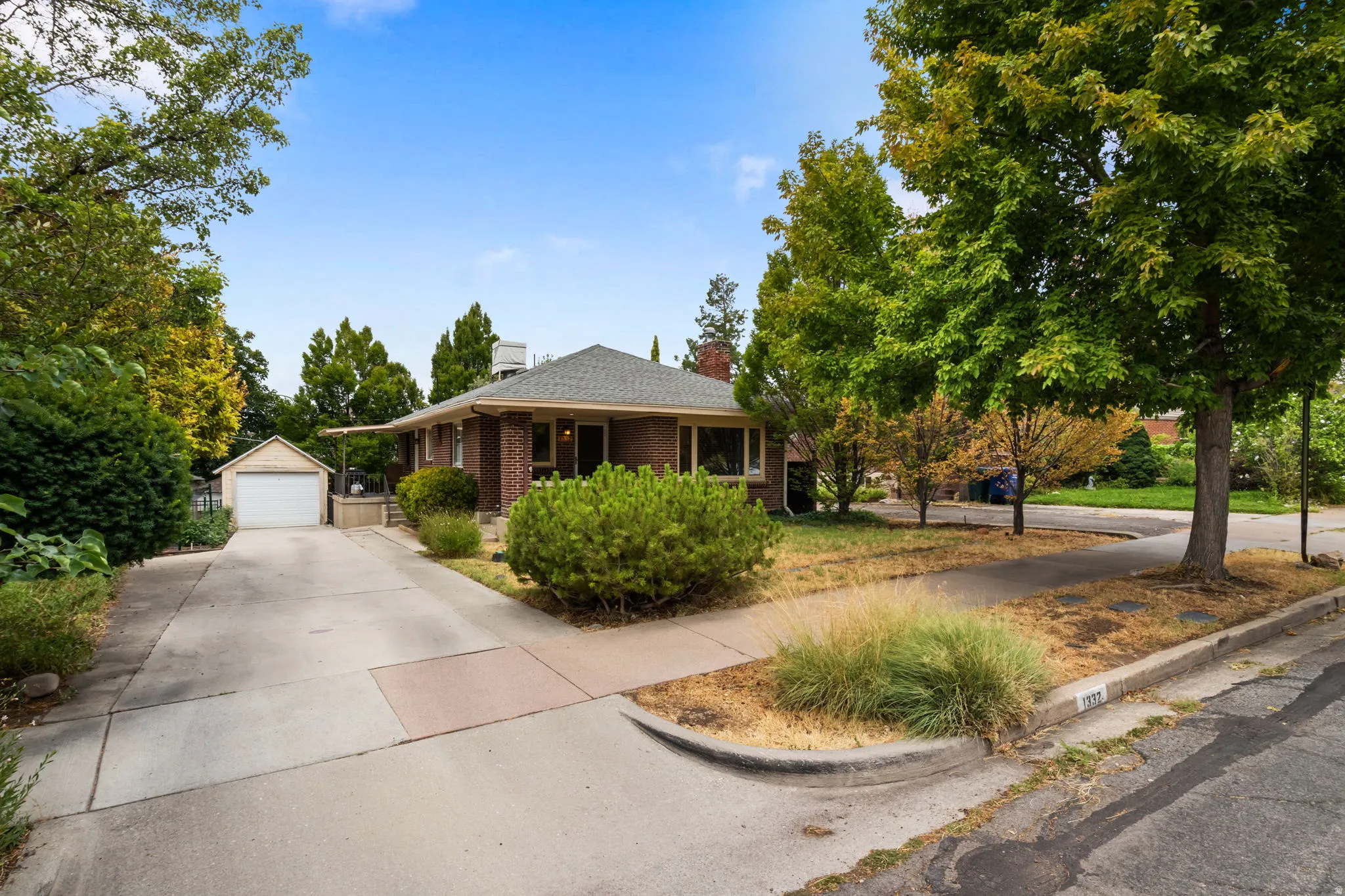 Brick exterior residence with a gabled roof, mature trees, and a detached garage featuring a white door