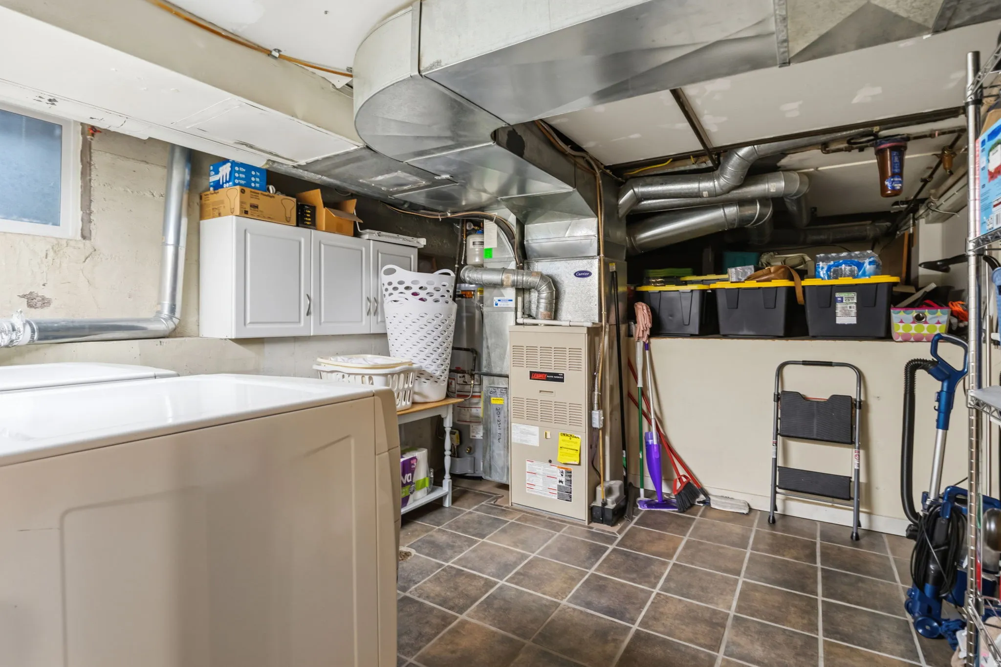 Laundry with basement shelf for storage. Utility space featuring ceramic tile flooring, built-in white cabinetry, a utility sink, and HVAC system