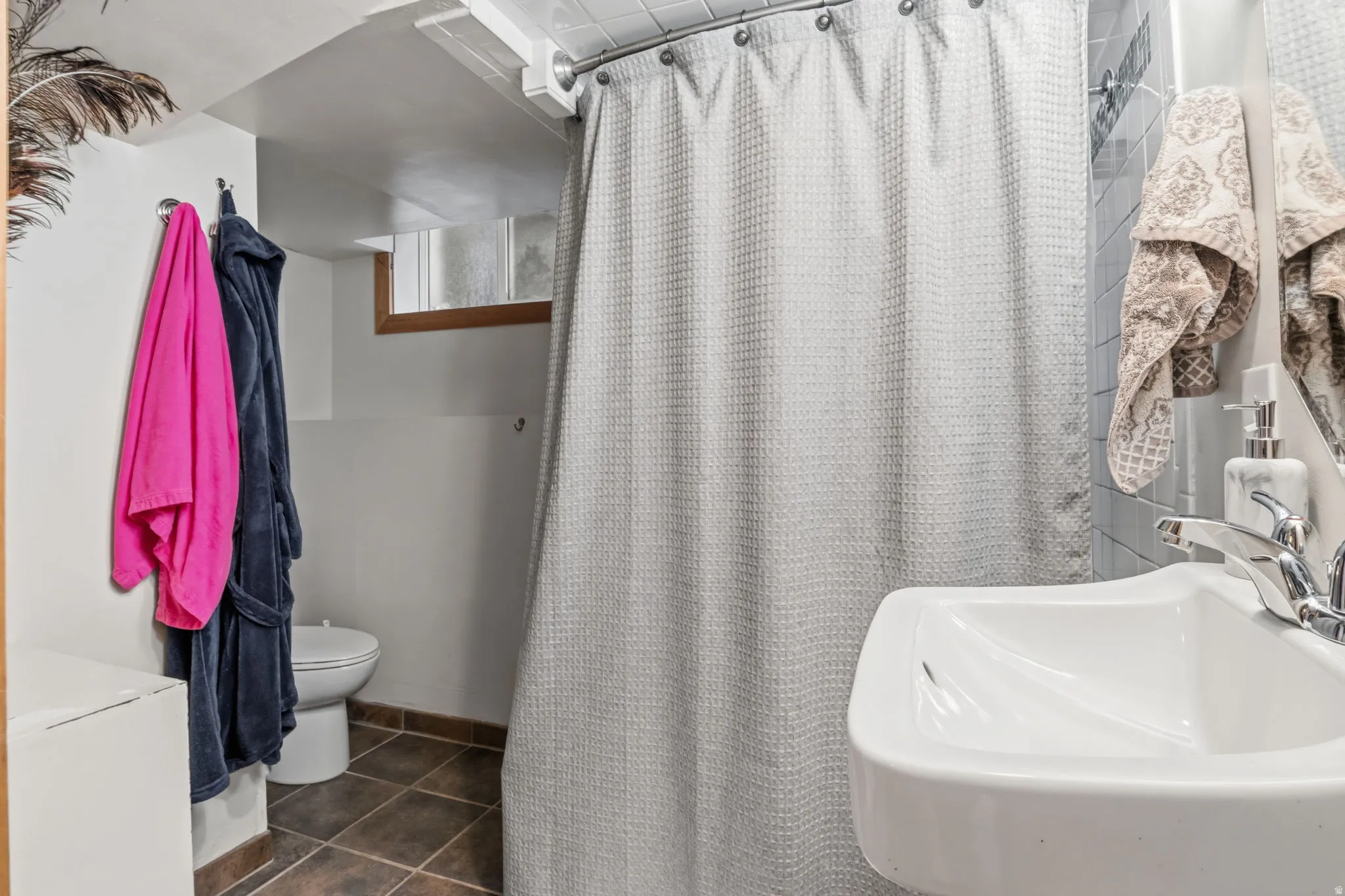 Wall-mounted sink with chrome faucet, tiled shower enclosure, and tiled flooring