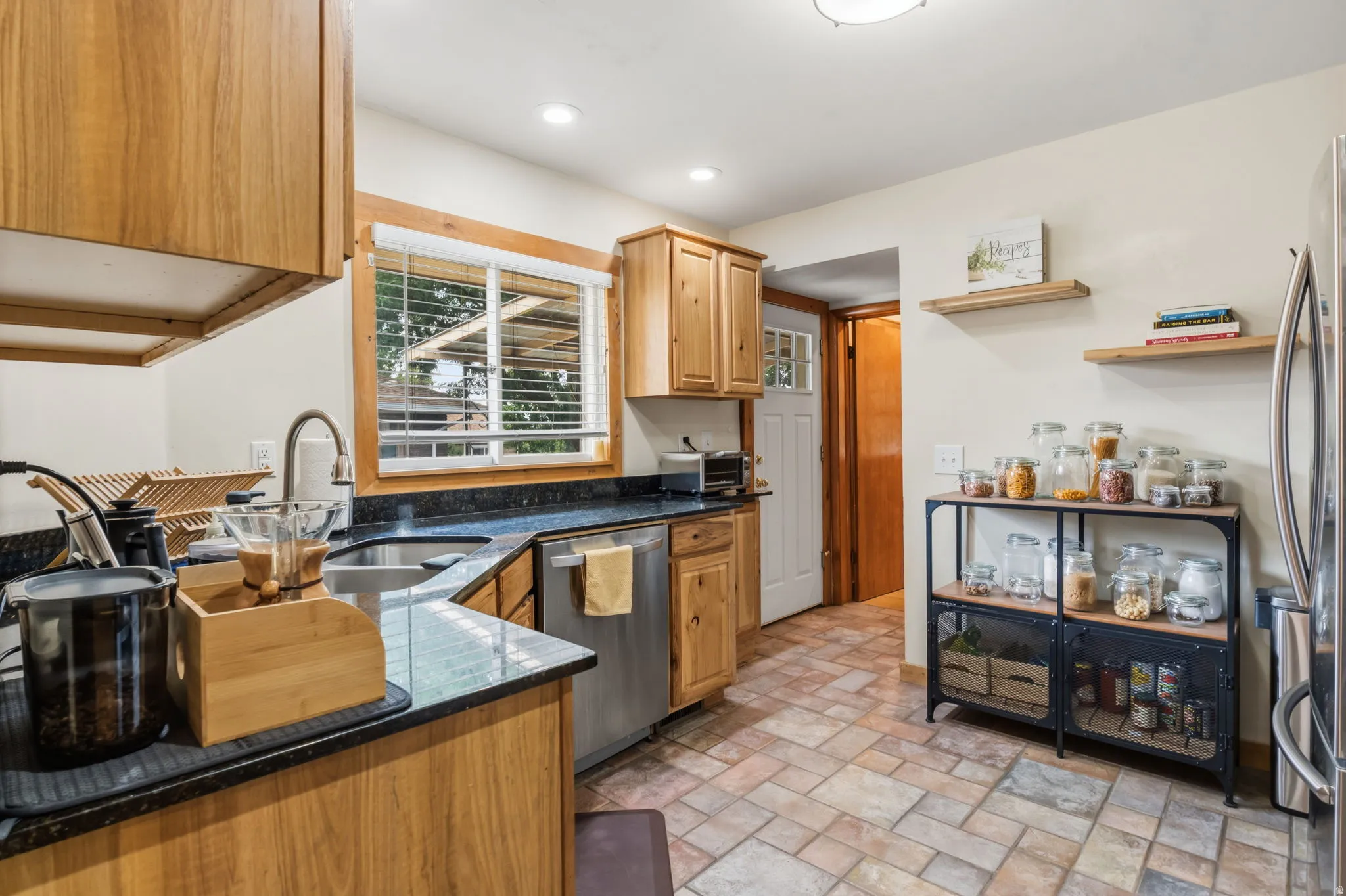 Kitchen featuring wood cabinetry, dark countertops, a stainless steel dishwasher, and tiled flooring