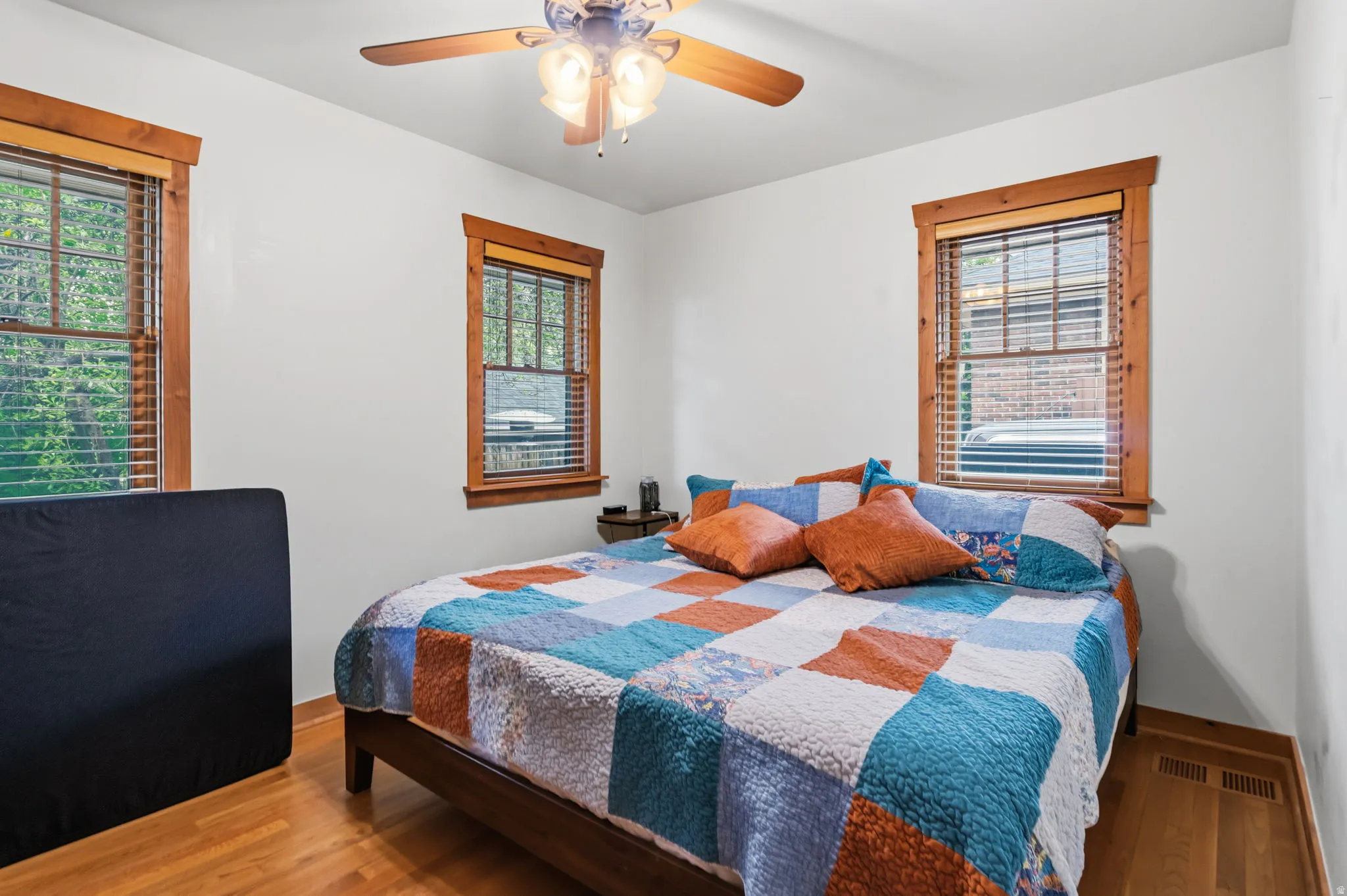 Wood-finish flooring, two windows with wood trim, ceiling fan light fixture, and white wall finishes