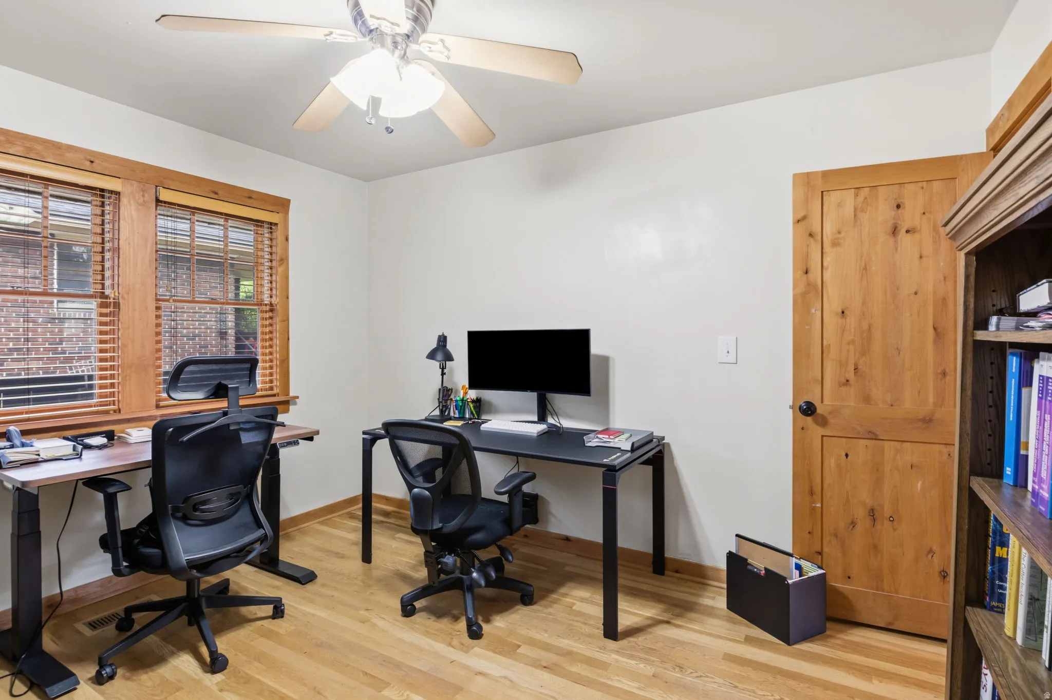 Hardwood flooring throughout, two windows with wood trim, wood paneled door, and a ceiling fan with light fixture