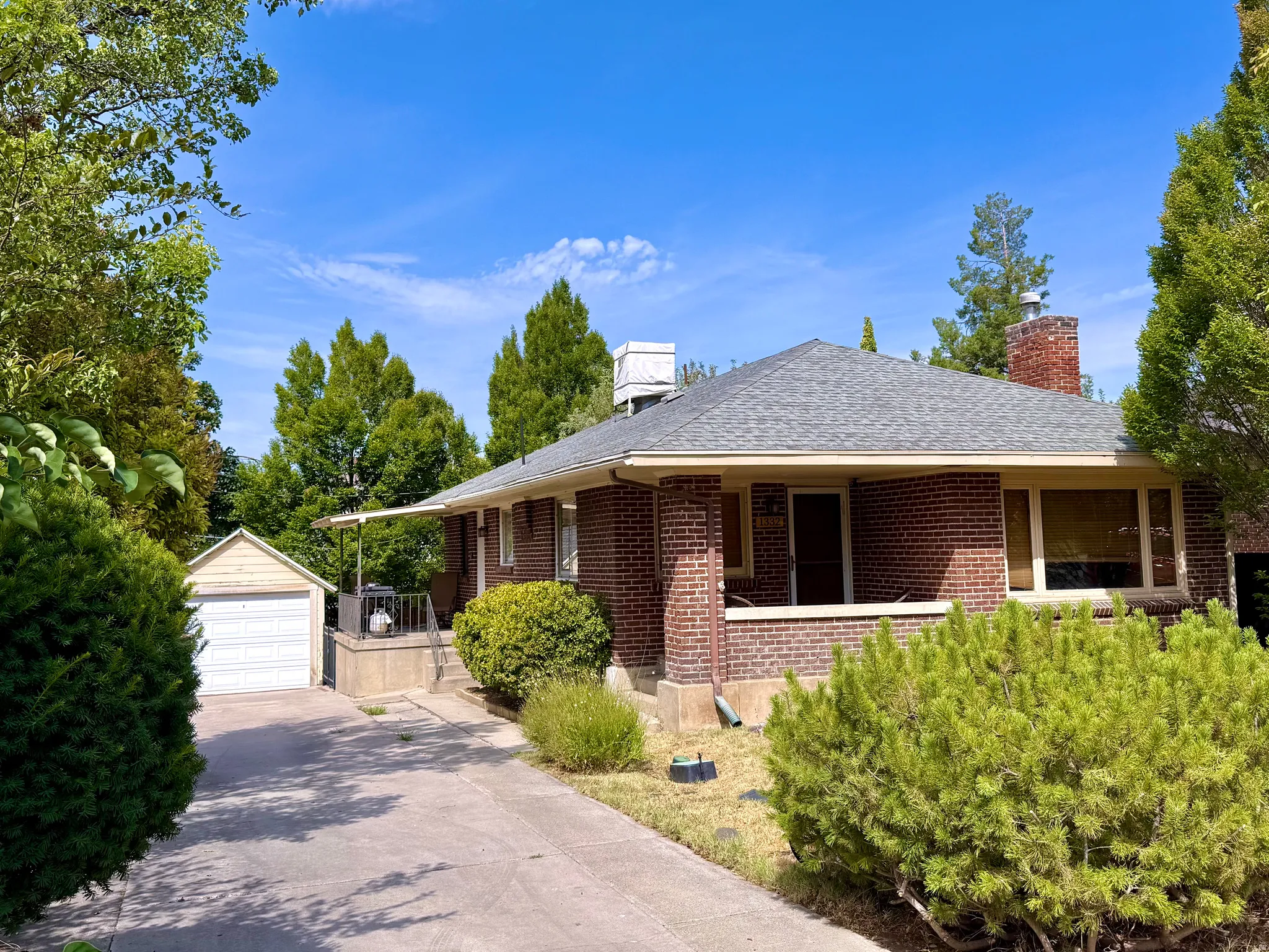 Brick exterior, covered front porch, attached chimney, shingled roof, and a detached garage