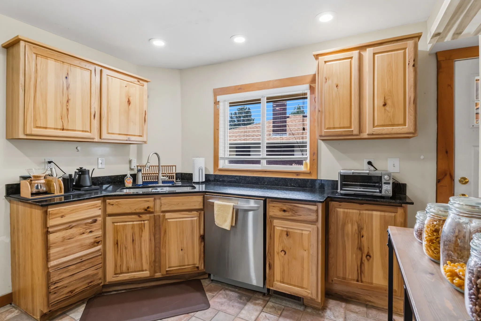 Kitchen featuring wood cabinetry, dark countertops, a stainless steel dishwasher, and a window with blinds