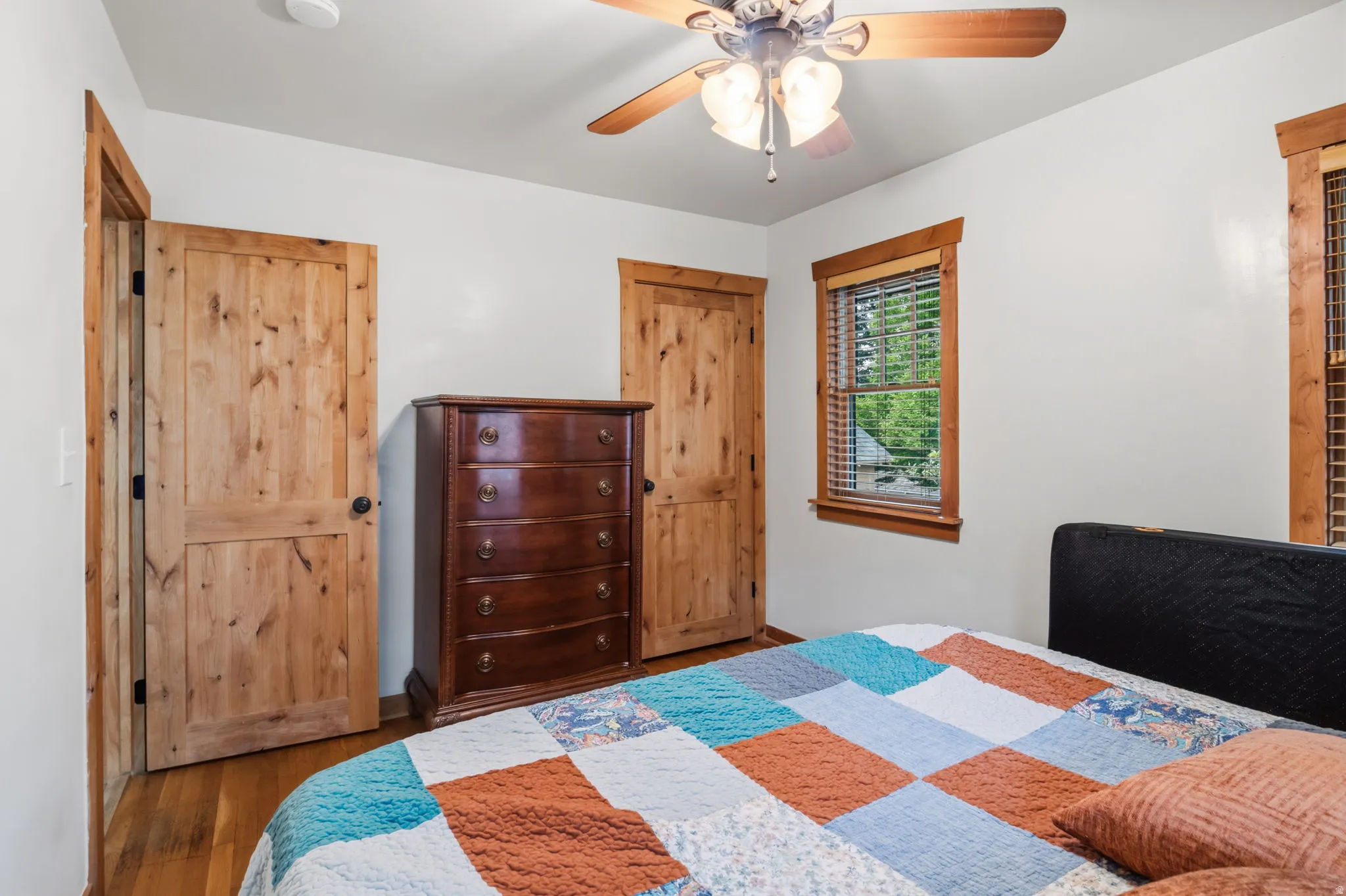 Wood-finish flooring, natural wood doors and trim, ceiling fan with light fixture, and window with blinds