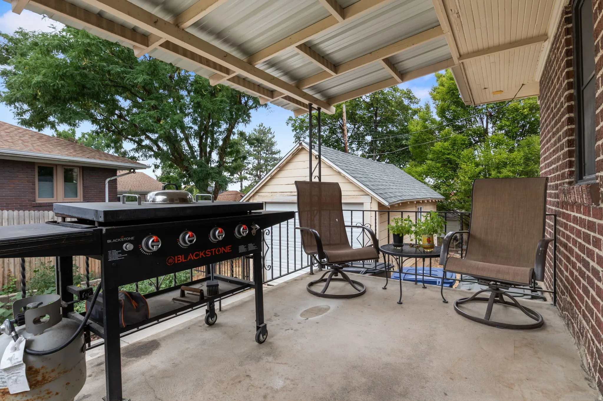 Patio by back garage. key box on railing. Covered outdoor patio with a concrete surface, brick exterior wall, and ornamental metal railing