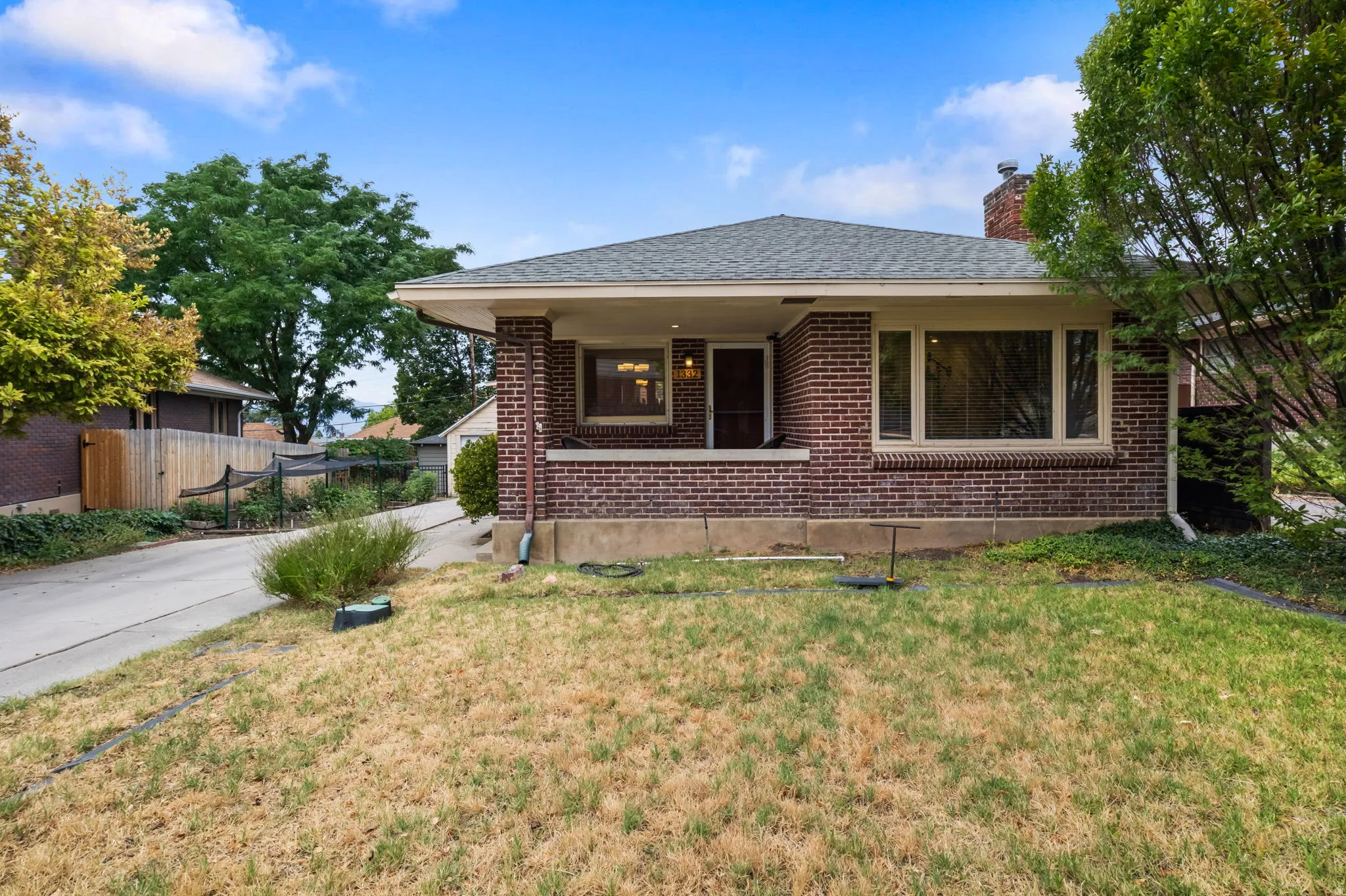 Brick exterior, covered front porch, multiple windows, gabled roof, and mature perimeter trees