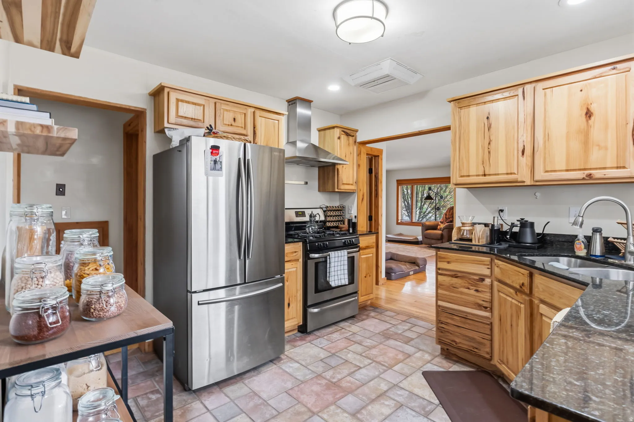 Kitchen featuring natural wood cabinetry, stainless steel appliances, dark stone countertops, and multi-toned tile flooring