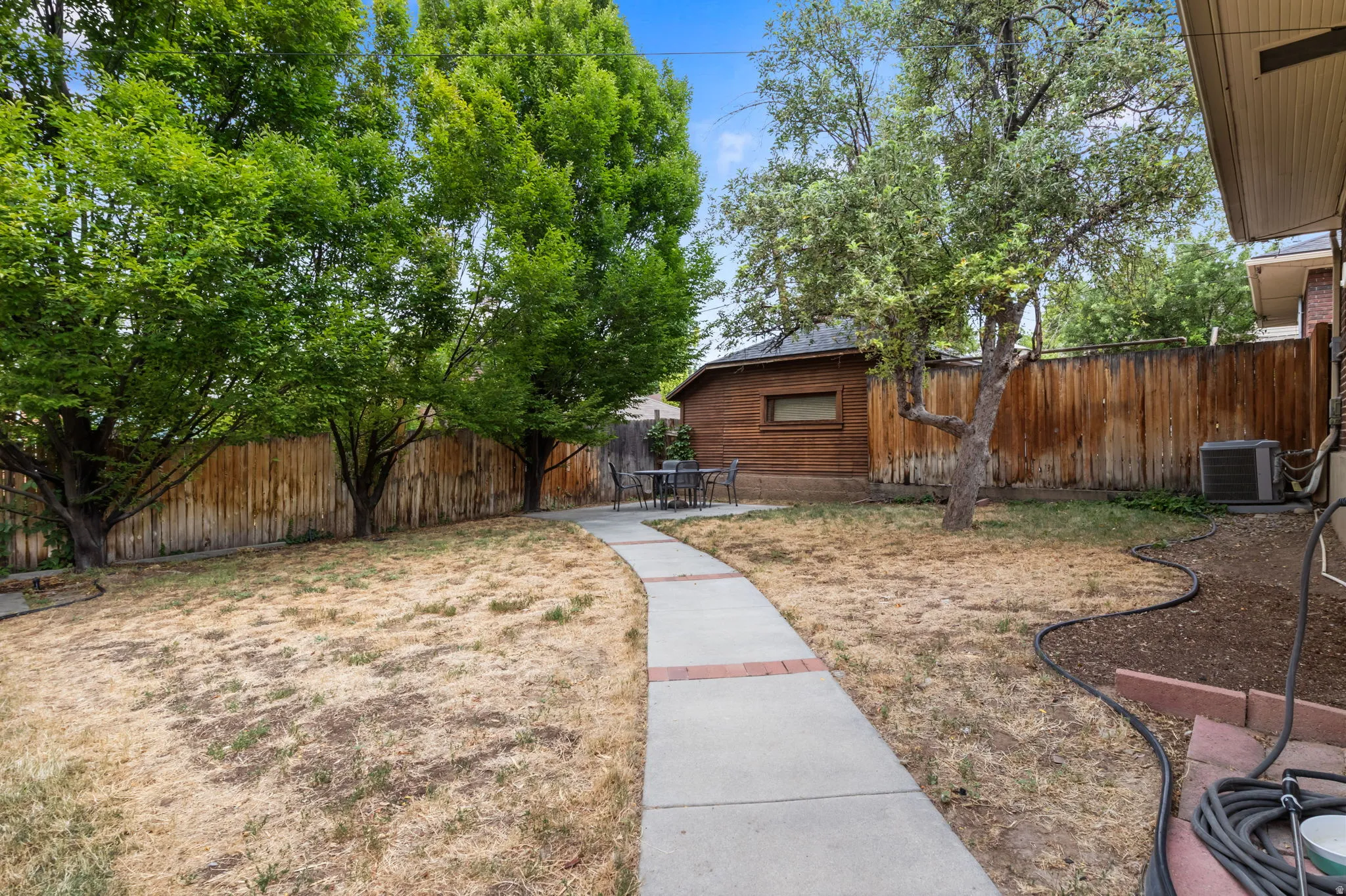 Amazing secluded Expansive backyard featuring a curved concrete walkway with brick accents, mature trees, and a wooden privacy fence