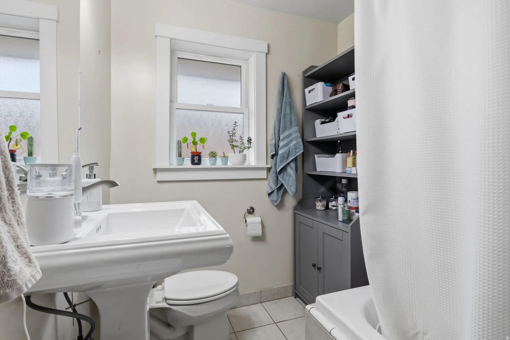 Pedestal sink with chrome faucet, multiple windows, and a built-in storage cabinet with open shelving