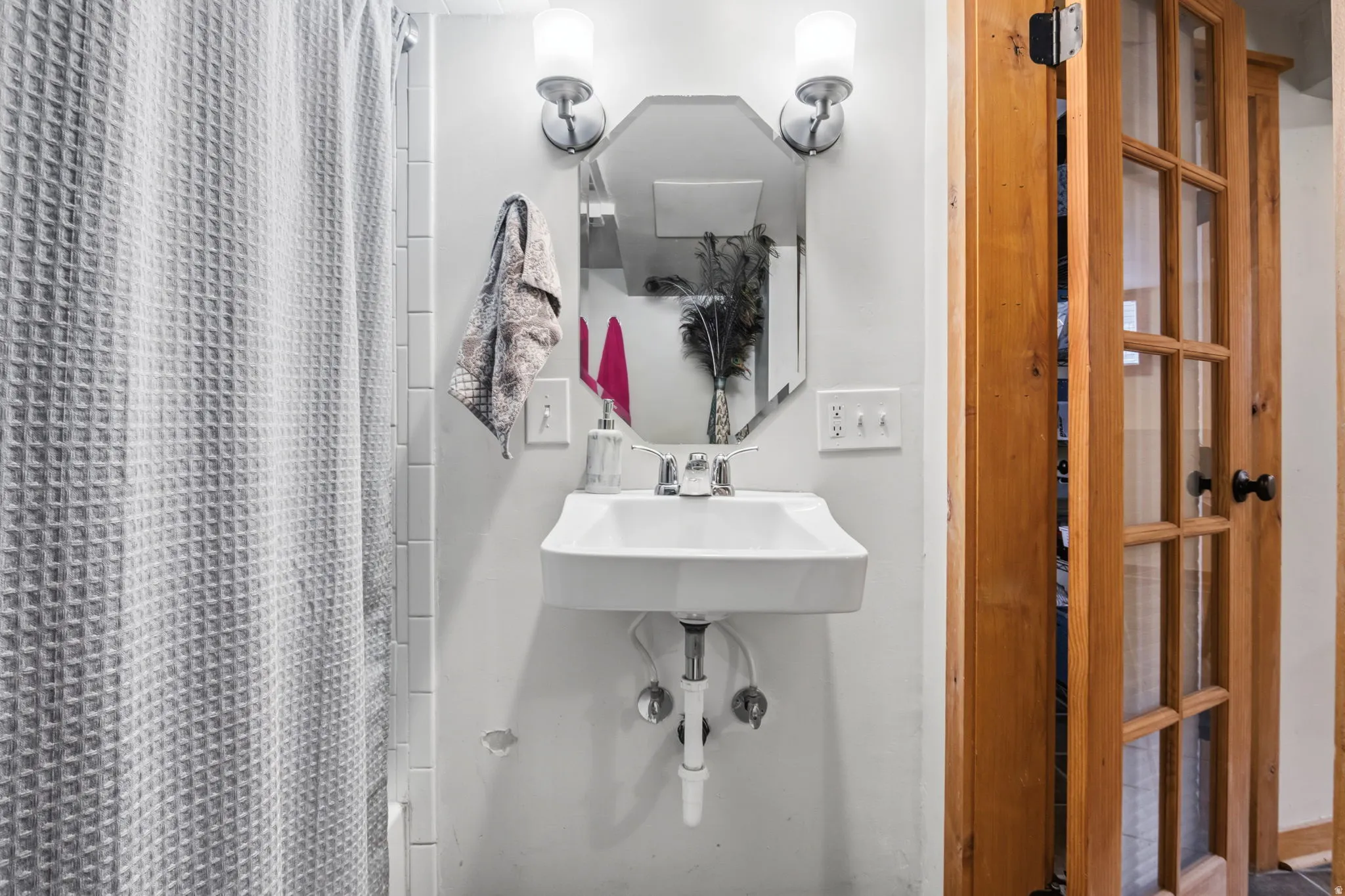 Wall-mounted sink with chrome faucet, flanked by dual wall sconces and a decorative mirror