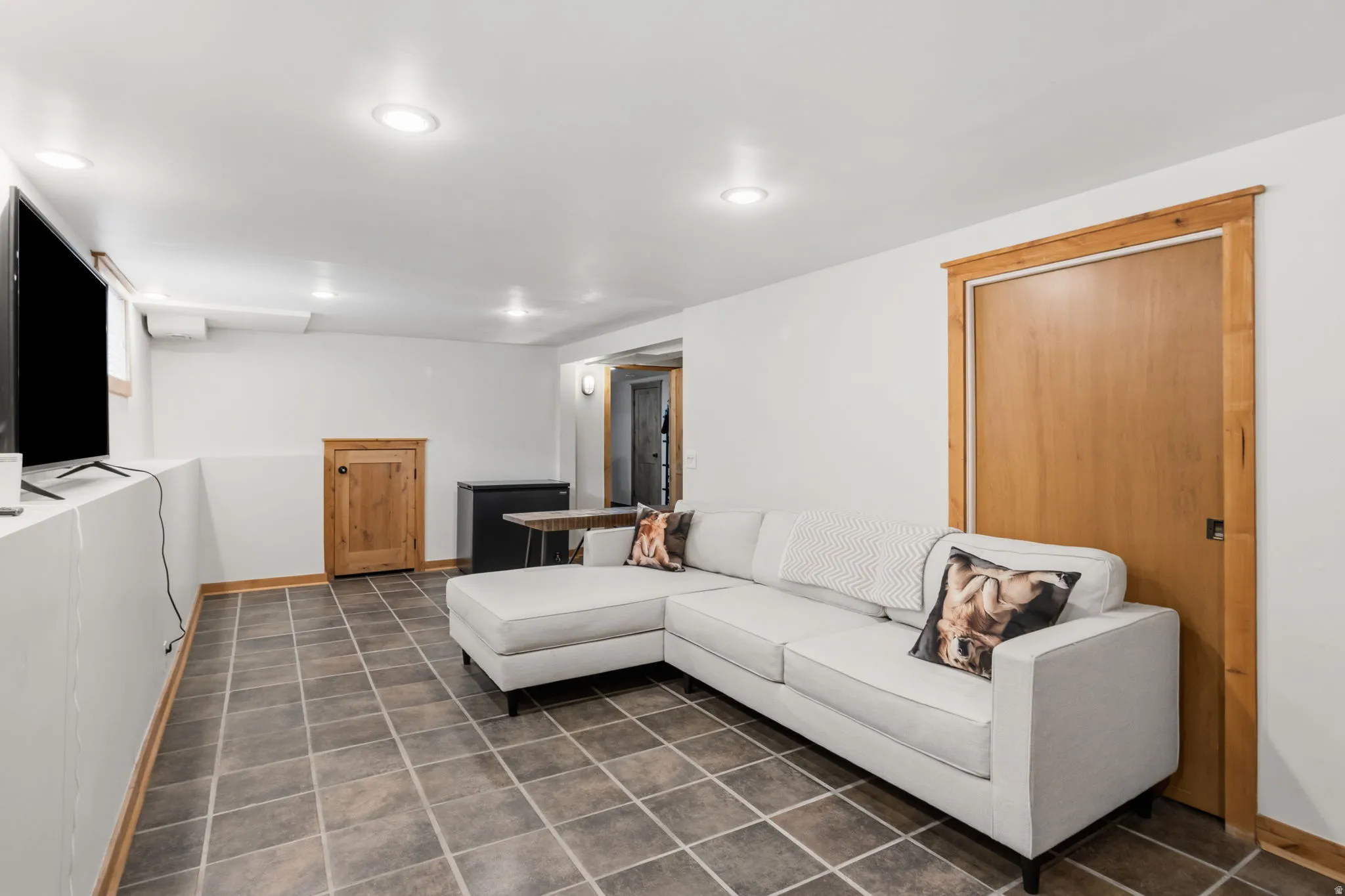 Living room and storage under stairs. Recessed ceiling lighting, tiled flooring, wood-finish door, and wood-finish trim