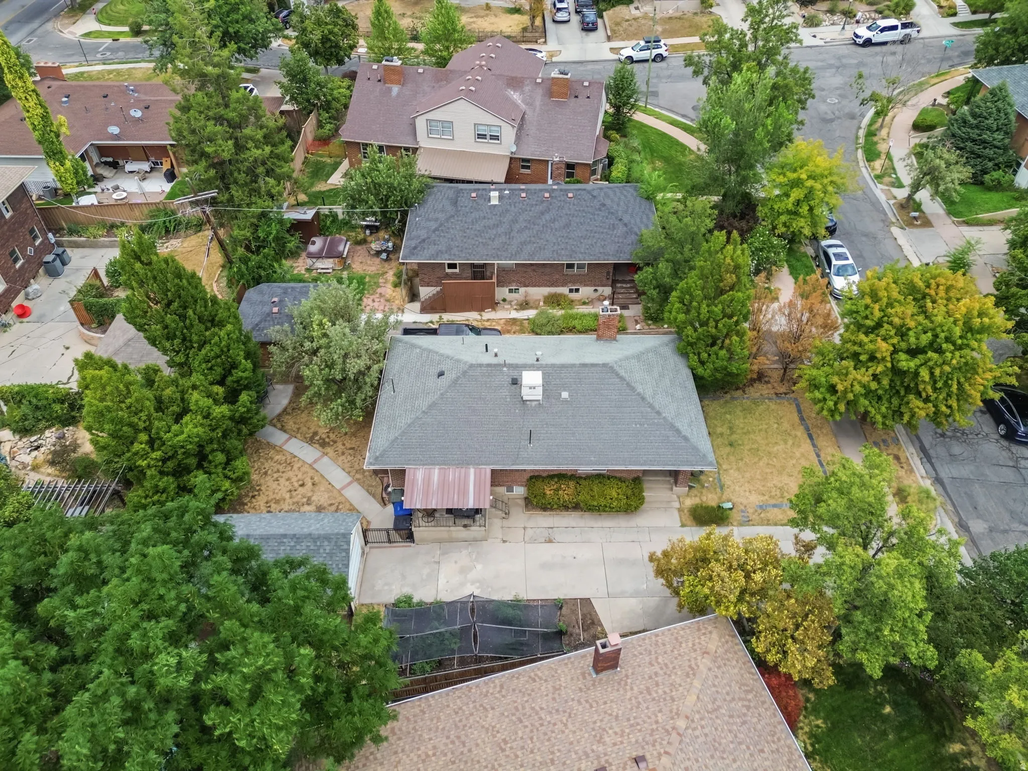 Gabled roofline, concrete driveway, attached carport, mature trees, and an additional shed structure
