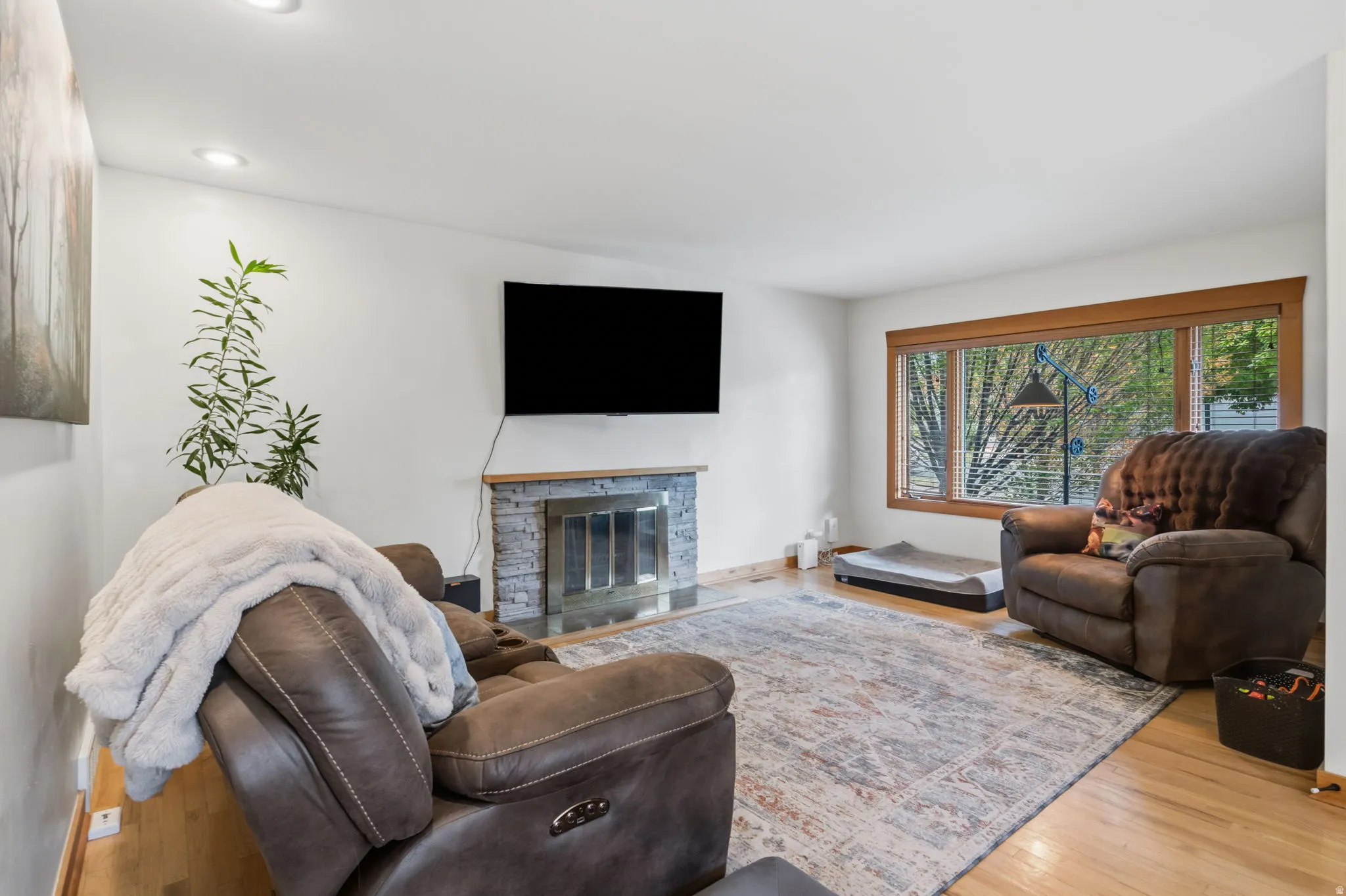 Recessed lighting, wood-finish flooring, and a stone-clad fireplace with a hearth