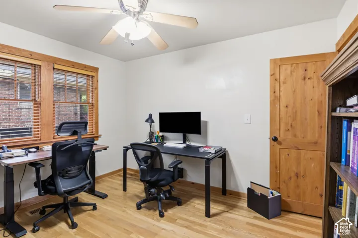 Hardwood flooring throughout, two windows with wood trim, wood paneled door, and a ceiling fan with light fixture
