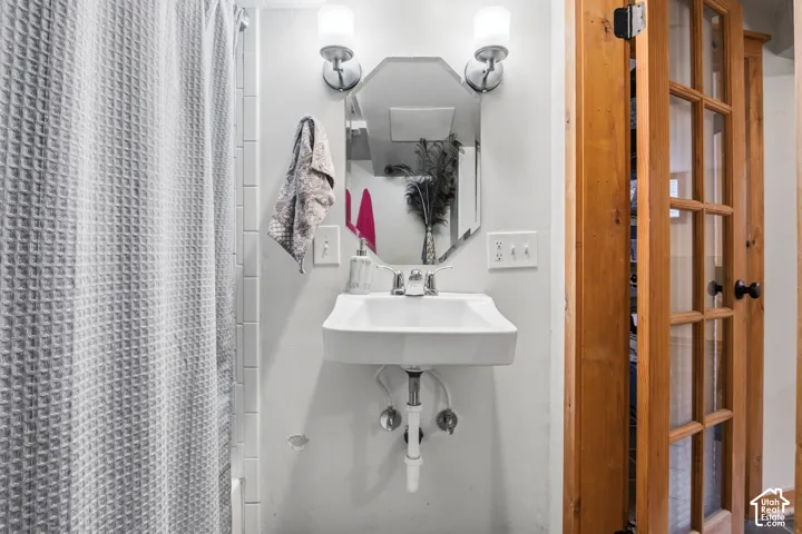 Wall-mounted sink with chrome faucet, flanked by dual wall sconces and a decorative mirror