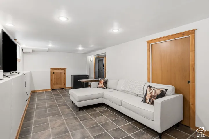 Living room and storage under stairs. Recessed ceiling lighting, tiled flooring, wood-finish door, and wood-finish trim