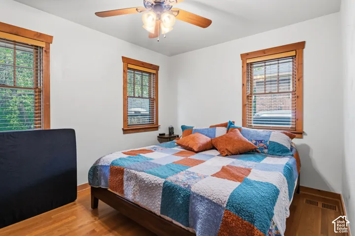 Wood-finish flooring, two windows with wood trim, ceiling fan light fixture, and white wall finishes