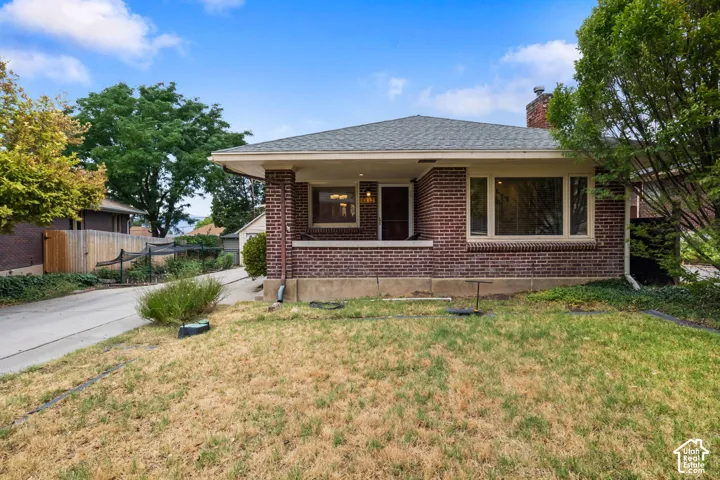 Brick exterior, covered front porch, multiple windows, gabled roof, and mature perimeter trees