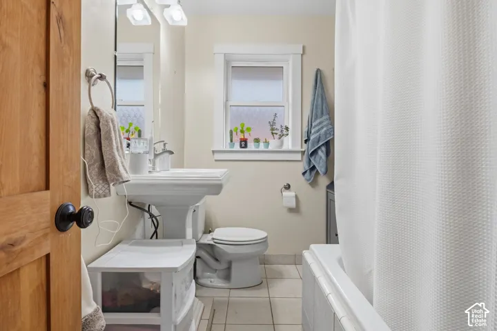 Pedestal sink with chrome faucet, tiled flooring, window with frosted glass, and white bathtub with tiled surround