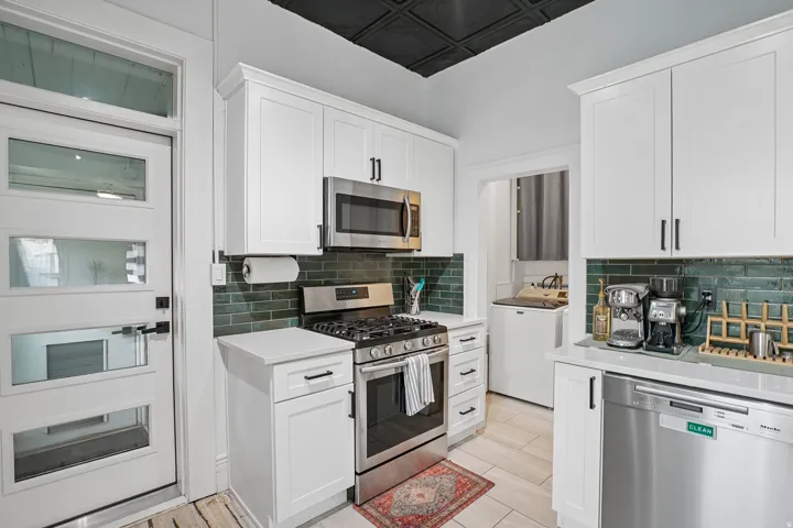 White shaker-style cabinetry with matte black hardware, stainless steel appliances, and a dark green subway tile backsplash