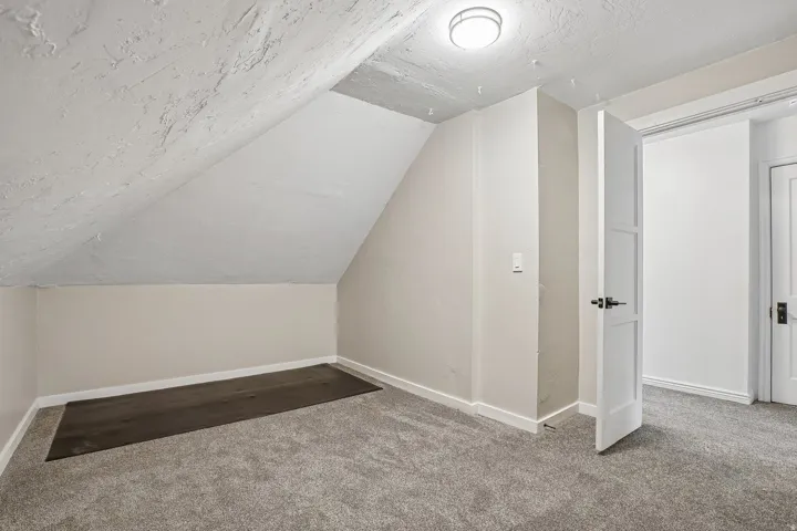 Spacious attic room with sloped ceilings, neutral wall finishes, and plush carpeting throughout