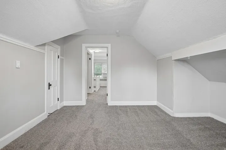 Carpeted flooring with painted walls, a white door with black hardware, and an open doorway leading into another room