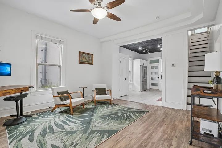 Wood-finish flooring, ceiling fan with integrated lighting, white trim and baseboards, and a staircase with contrasting risers