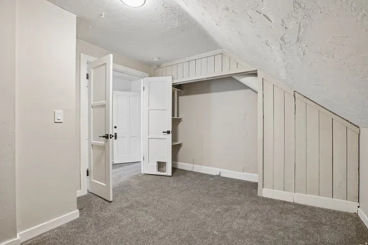 Sloped ceiling bedroom featuring gray carpet, built-in closet shelving, and a paneled door