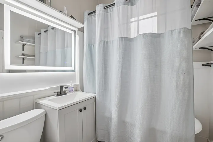 Modern bathroom featuring a floating vanity with white cabinetry and a rectangular vessel sink, LED-illuminated mirror with integrated lighting, polished chrome fixtures, and a glass-enclosed shower with subway tile surround and clear glass enclosure