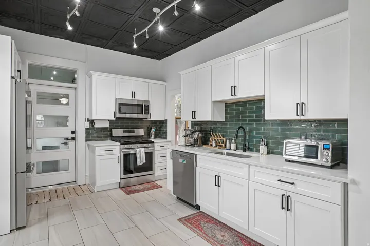 Modern kitchen featuring white shaker cabinetry, stainless steel appliances, a green subway tile backsplash, white countertops, and light-toned tile flooring