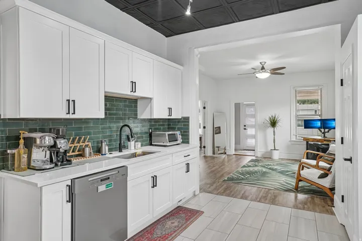 Kitchen featuring white shaker cabinetry, subway tile backsplash, stainless steel dishwasher, a single basin sink with a gooseneck faucet, and a decorative ceiling