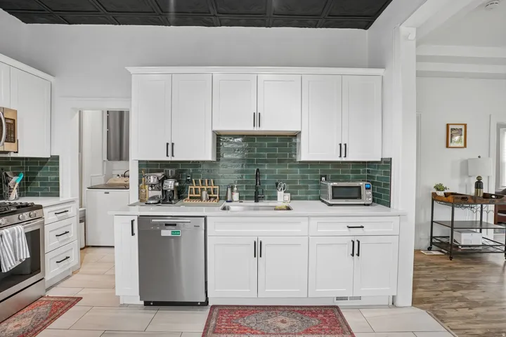 White shaker cabinetry, stainless steel appliances, subway tile backsplash, solid surface countertops, and a black decorative ceiling