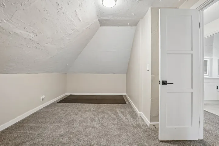 Sloped ceiling detail with recessed lighting, gray carpeted flooring, white trim, and a three-panel door with matte black hardware