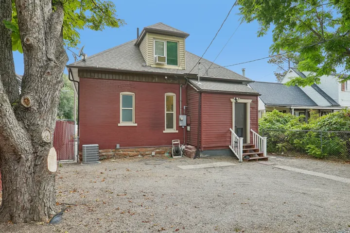 Red brick and siding exterior with a dormer window, gravel ground cover, and a chain-link fence